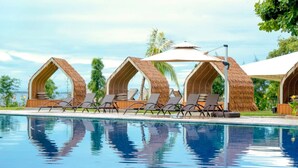 A poolside area with thatched-roof cabanas and lounge chairs.