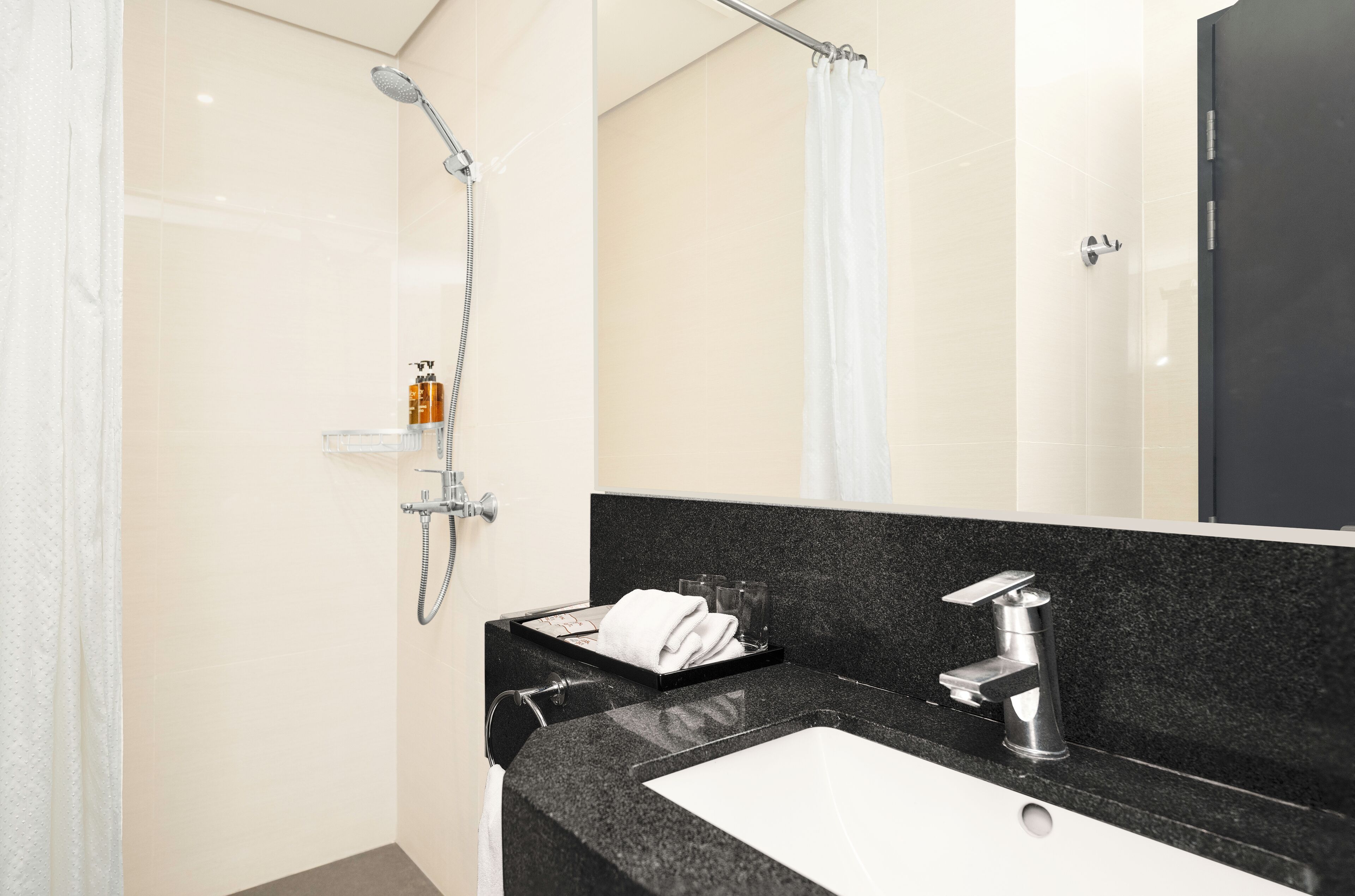 A modern bathroom with a black countertop, a white sink, a shower with a handheld showerhead, and a glass shower enclosure.