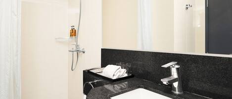 Une salle de bain moderne avec un plan de toilette noir, un lavabo blanc, une douche équipée d’un pommeau de douche à main et une paroi de douche en verre.