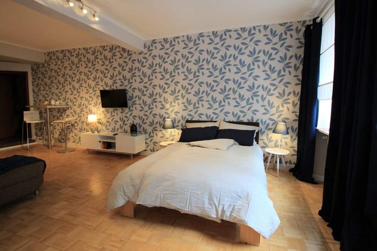 Une chambre à coucher avec un lit, des tables de chevet, une télévision et un mur décoré d’un motif.