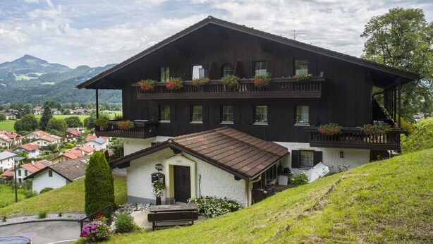 A two-story chalet with a sloped roof, wooden balconies with flower boxes, and a small attached building with a tiled roof. - Vacation apartment 2-5 persons in Oberaudorf ,sauna,playroom,fitness room/16 (Oberaudorf)