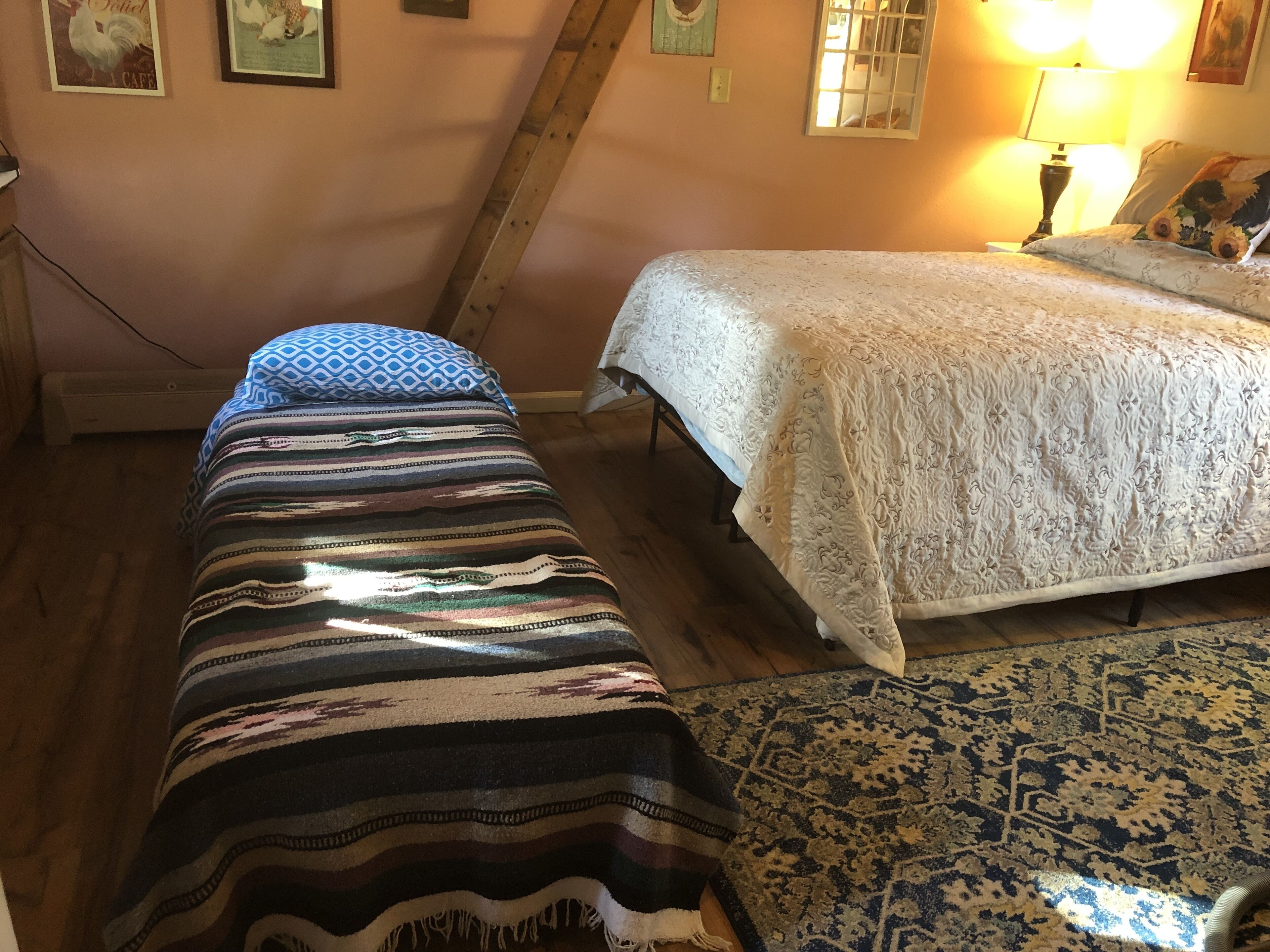 Quarto com duas camas, uma escada de madeira, um tapete estampado e uma parede com quadros.