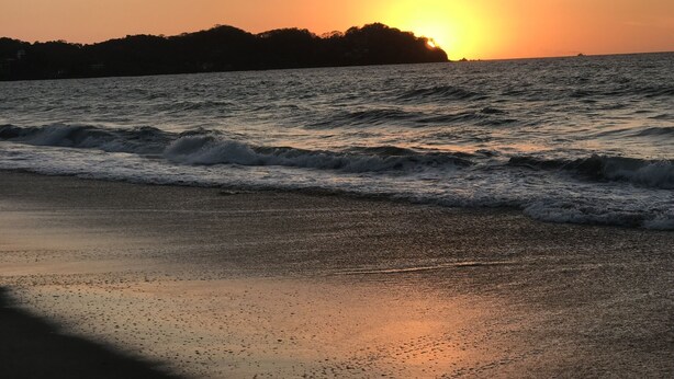 Ein Strand bei Sonnenuntergang, mit Wellen.