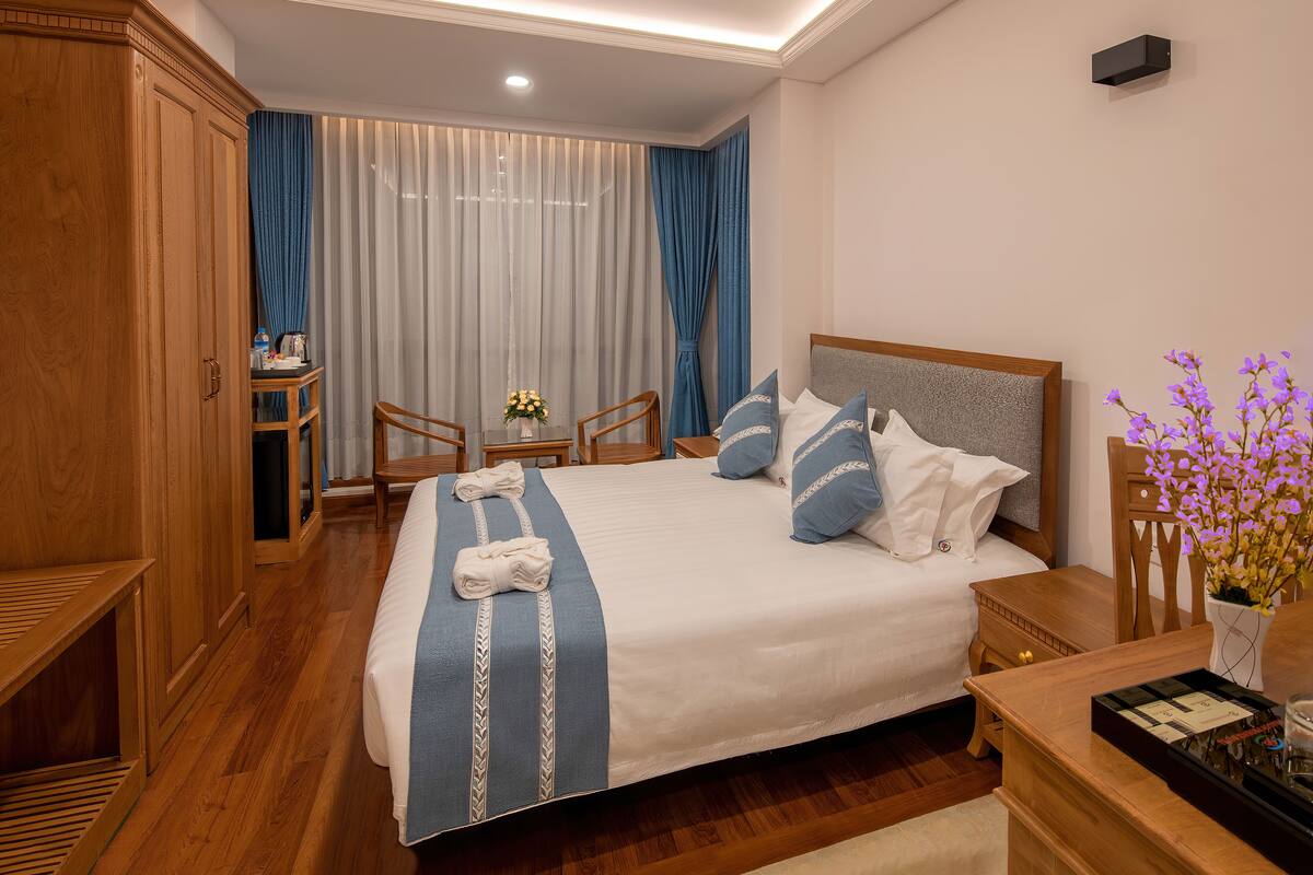 A neatly arranged hotel room with a large bed, wooden furniture, and a small table with a vase of flowers.