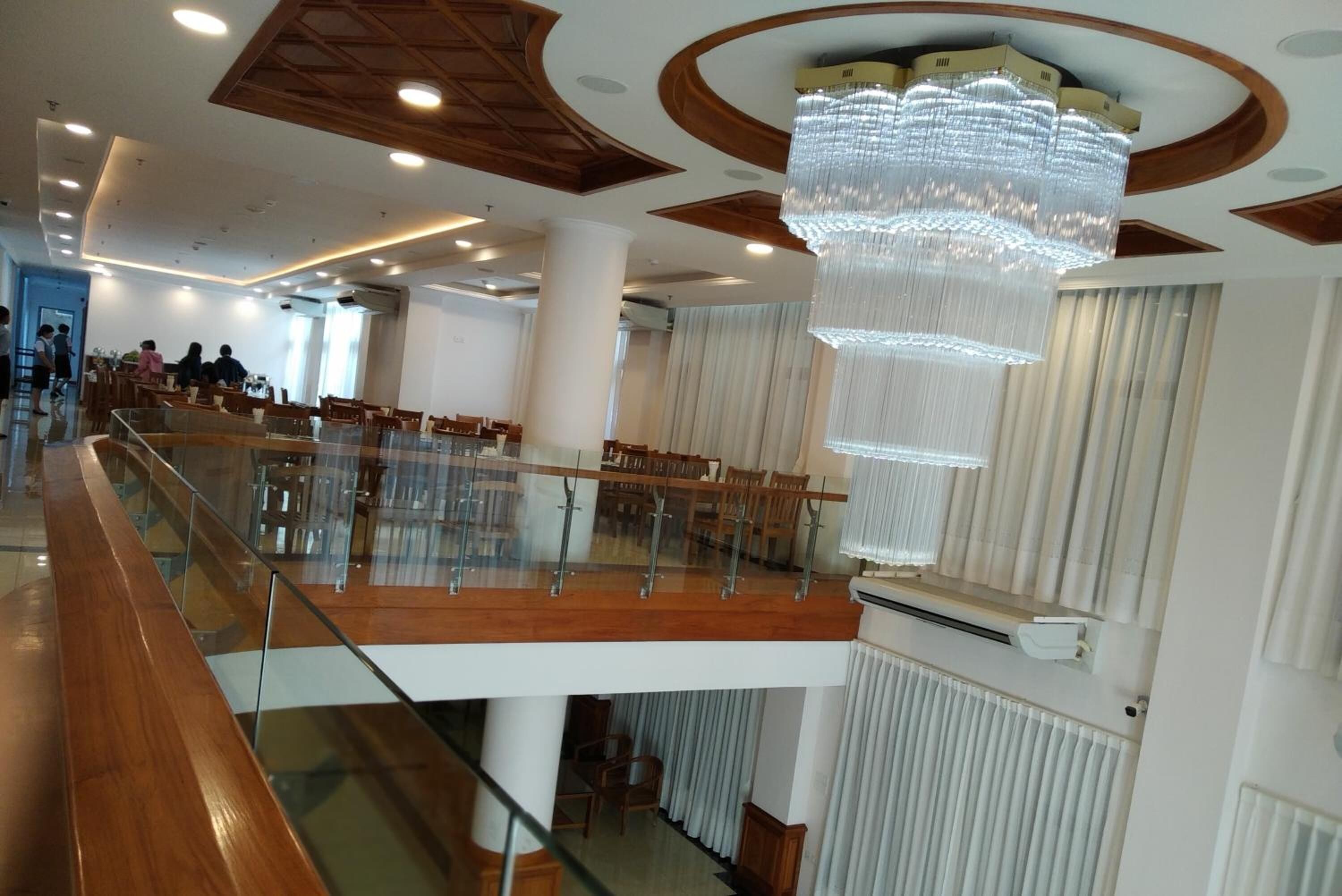 A spacious hotel lobby with a high ceiling, a large chandelier, and a glass railing overlooking the seating area.
