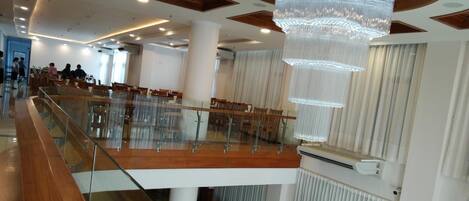 A spacious hotel lobby with a high ceiling, a large chandelier, and a glass railing overlooking the seating area.