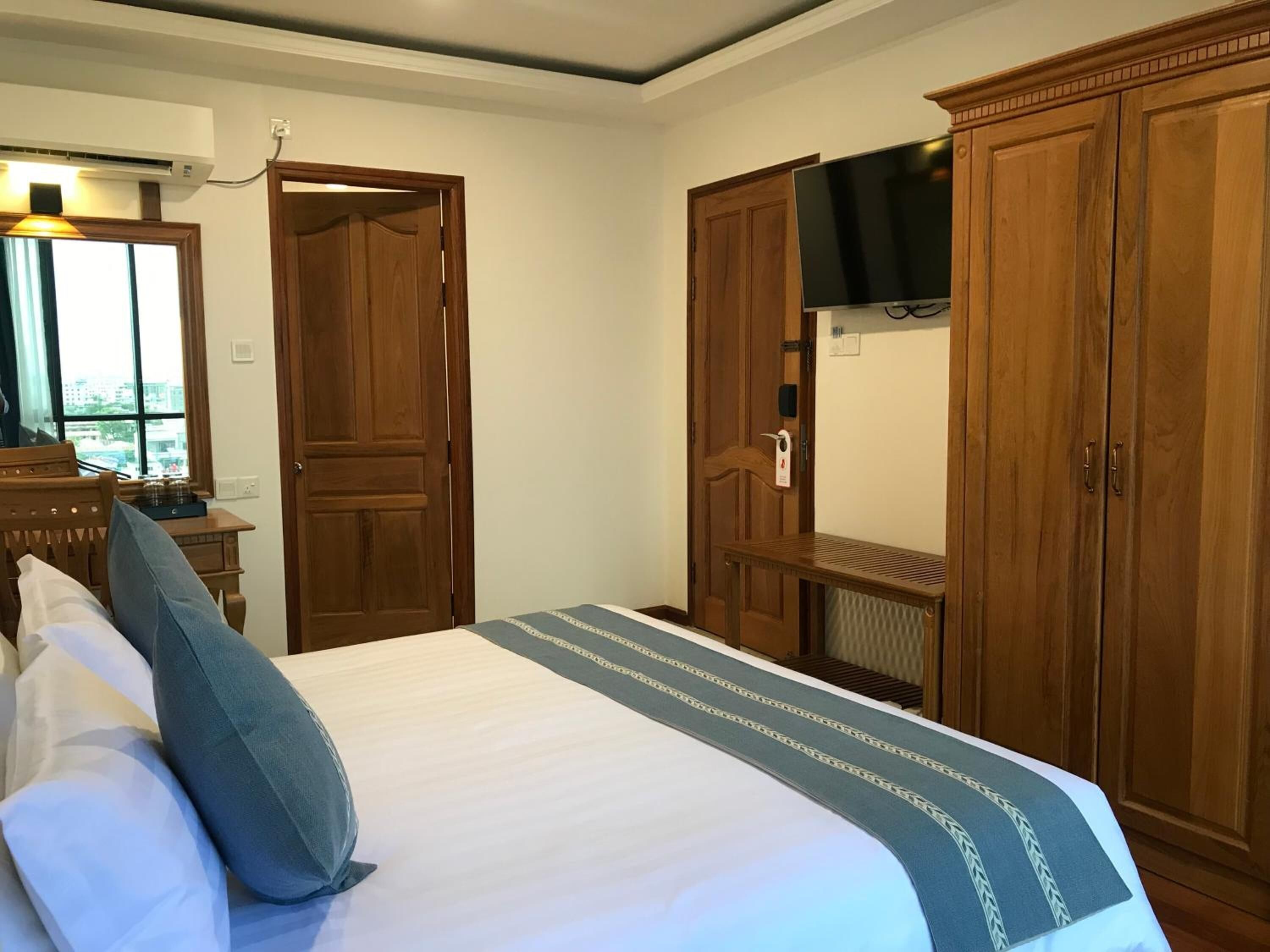 Habitación de hotel con cama, armario de madera, televisor montado en la pared y ventana con cortinas.