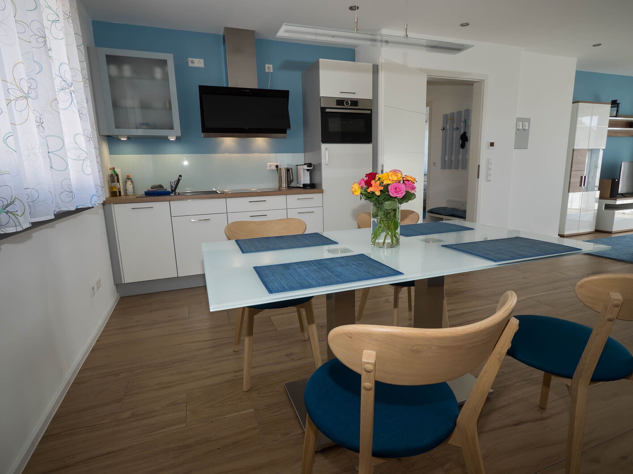 A modern kitchen with white cabinets, a built-in oven, and a flat-screen TV.
