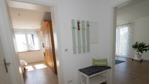 Ein Zimmer mit Holzboden, einer Bank mit Kissen, einem an der Wand befestigten Kleiderhaken und einer Topfpflanze.