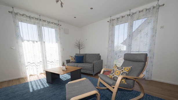 Ein Wohnzimmer mit grauem Sofa, einem Holztisch, einem Schaukelstuhl und einem blauen Teppich.
