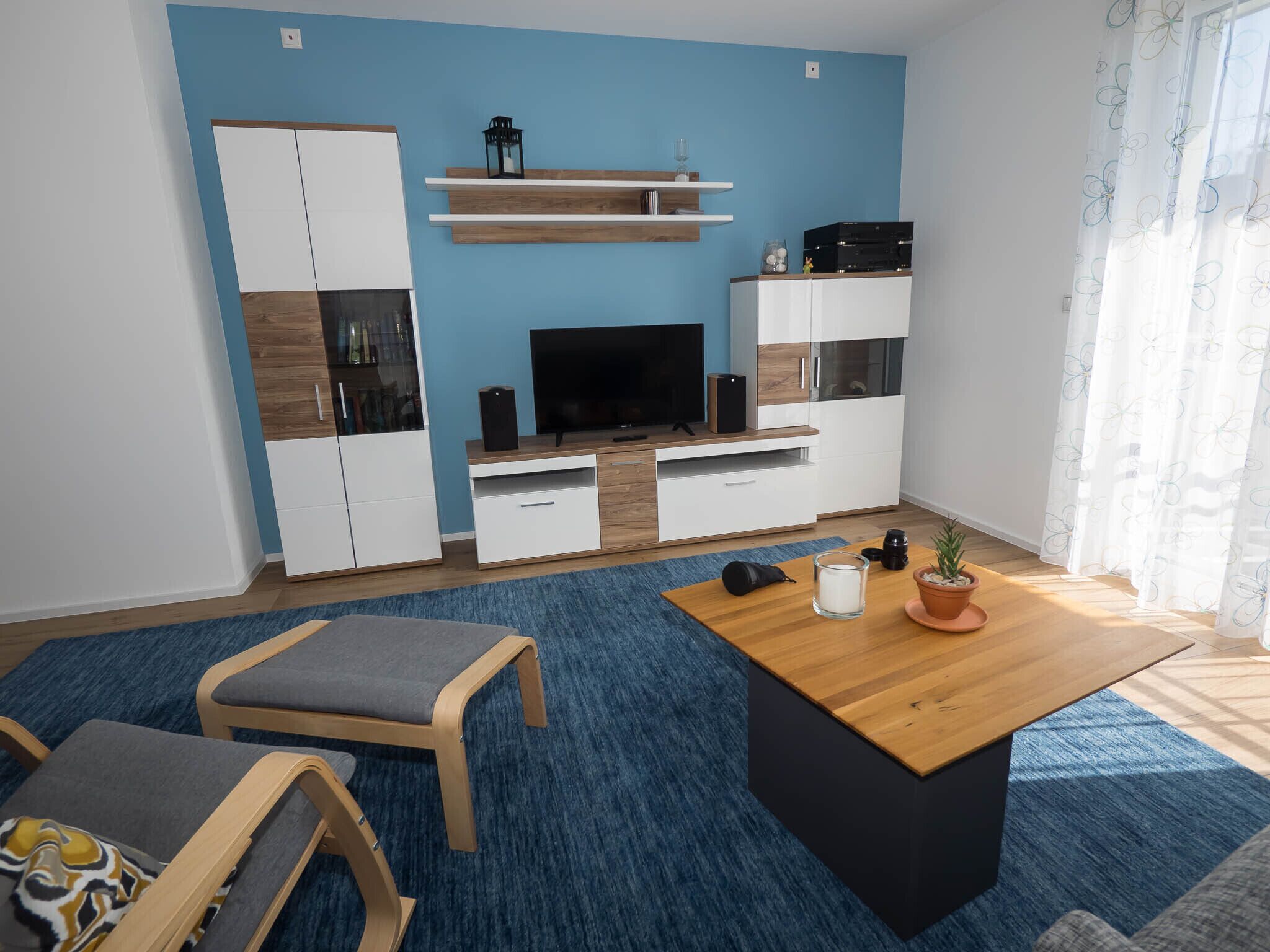 Un salon moderne avec un téléviseur, des meubles en bois, une table basse et un tapis bleu.