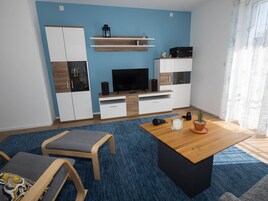 Una sala de estar moderna con televisor, armarios de madera, una mesa de centro y una alfombra azul.