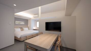 Una habitación de hotel moderna con una mesa de comedor de madera, dos camas individuales, un televisor de pantalla plana montado en la pared y un ventanal.