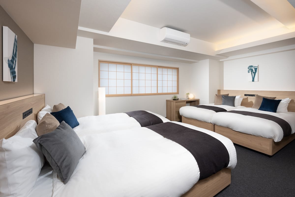 Ein Hotelzimmer mit zwei Betten, einem Shoji-Bildschirm, einem Schreibtisch mit Lampe und Kunstwerken an den Wänden.