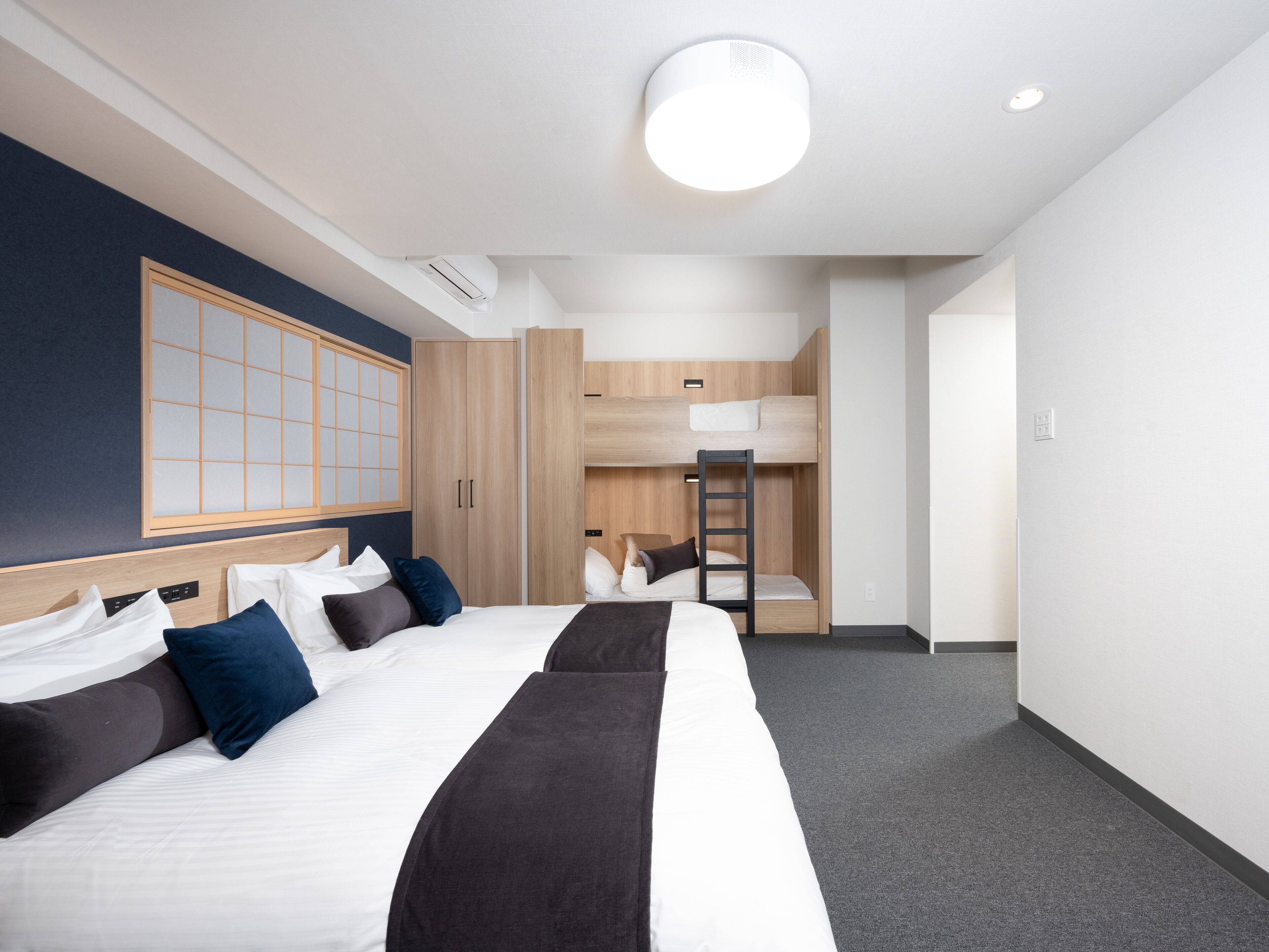 A modern hotel room with a large bed, a bunk bed, and a traditional-style wall panel.