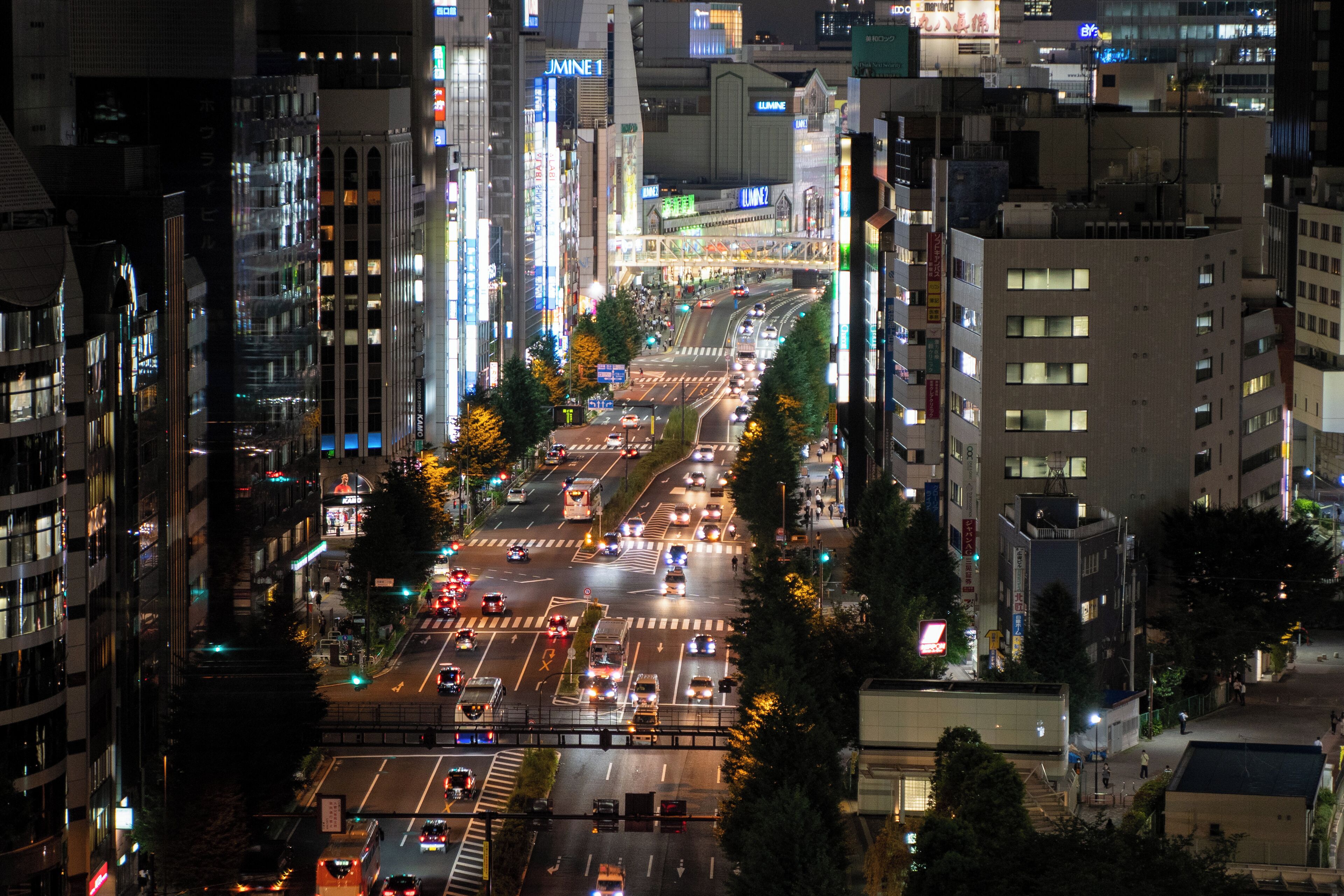 A nighttime cityscape with a busy intersection, illuminated buildings, and a pedestrian bridge.