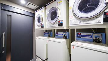 A laundry room with multiple washing machines and dryers, each labeled with numbers and instructions.