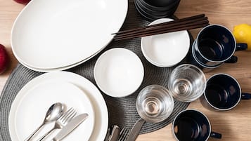 A table set with plates, bowls, chopsticks, and glasses, with apples and a lemon on the table.