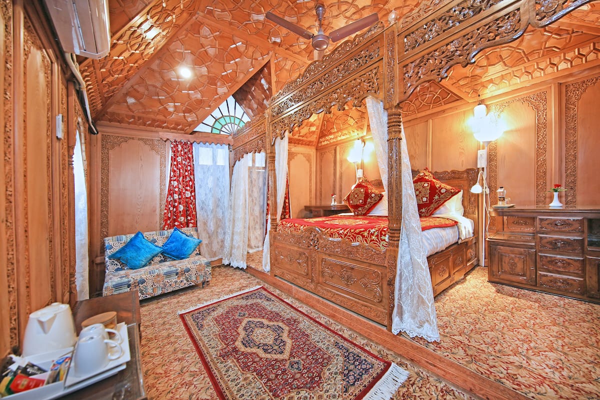 Una cama con dosel y ornamentales tallas, un techo de madera con diseños intrincados y una alfombra tradicional con motivos.