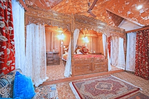 Una habitación tradicional con cama con dosel, techo de madera ornamentado y alfombras estampadas.