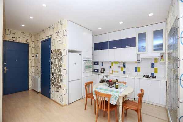 A compact kitchen with white cabinets, a blue door, and a dining area with a table set for two.
