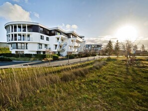 Un immeuble résidentiel moderne à plusieurs étages, doté de balcons, d’une façade incurvée et d’une pelouse bien entretenue en premier plan.