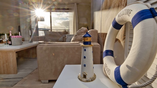 A cozy room with a white table, a small lighthouse model, and a lifebuoy with "WELCOME ABOARD" text.