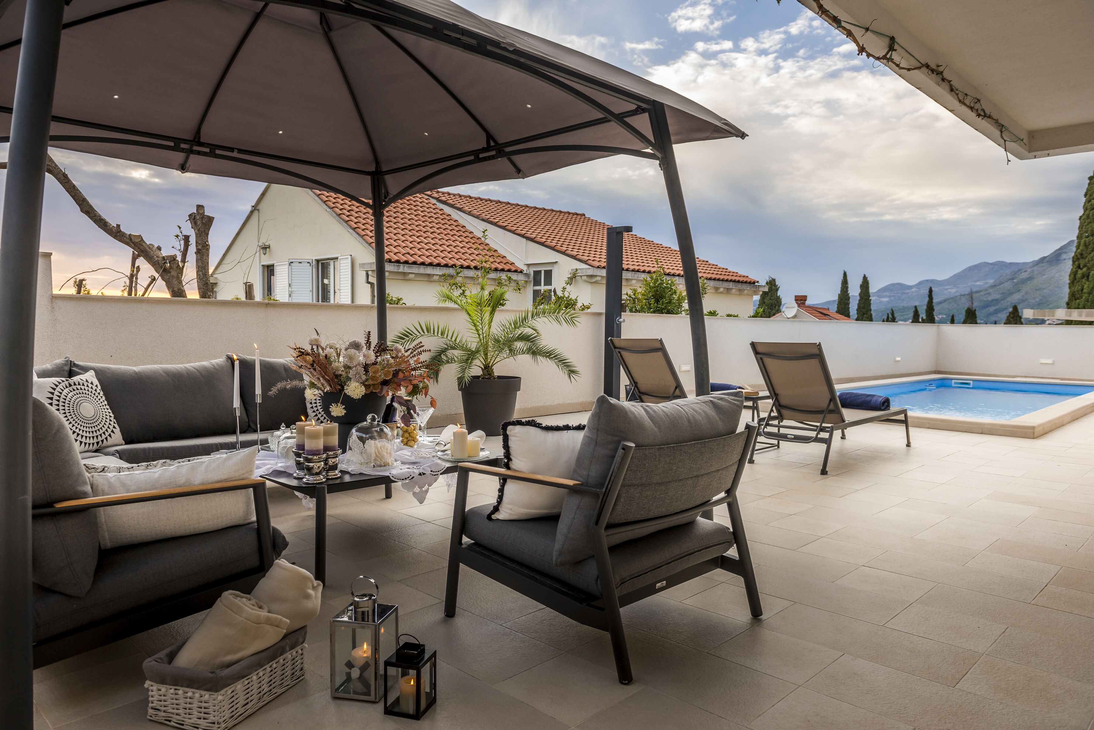 A covered outdoor seating area with a pool, a sofa, and a table with candles and flowers.