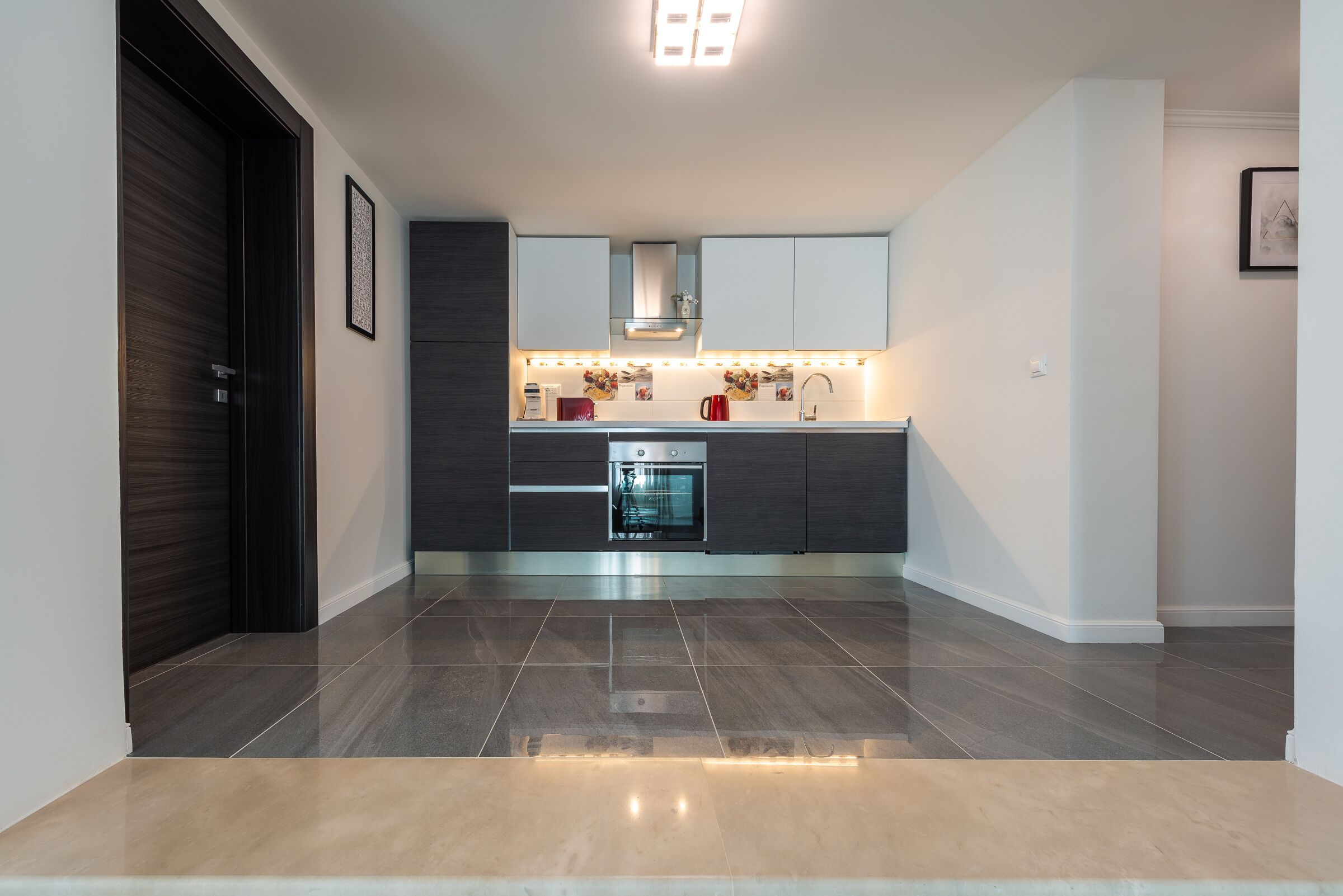 Une cuisine moderne avec des meubles de couleur sombre, un four en acier inoxydable et un éclairage sous les meubles.