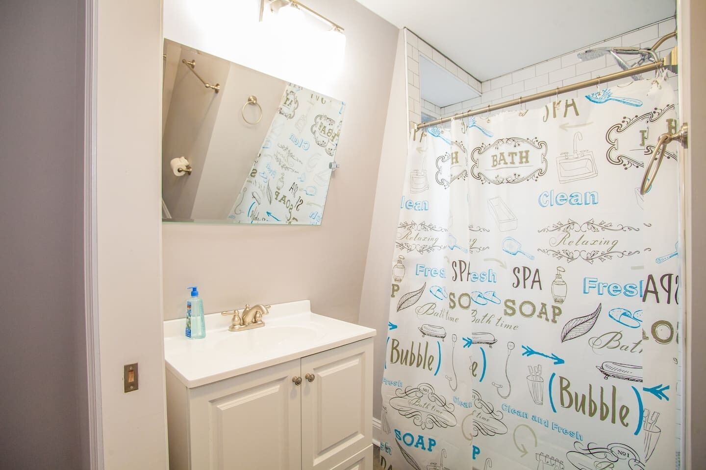 A bathroom with a white vanity, a mirror, and a shower curtain with spa-related illustrations.
