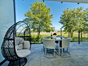 A patio with a round table and chairs, a hanging chair, and a view of trees and a fence.