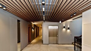 Um corredor moderno com teto de ripas de madeira, um elevador e uma escadaria.