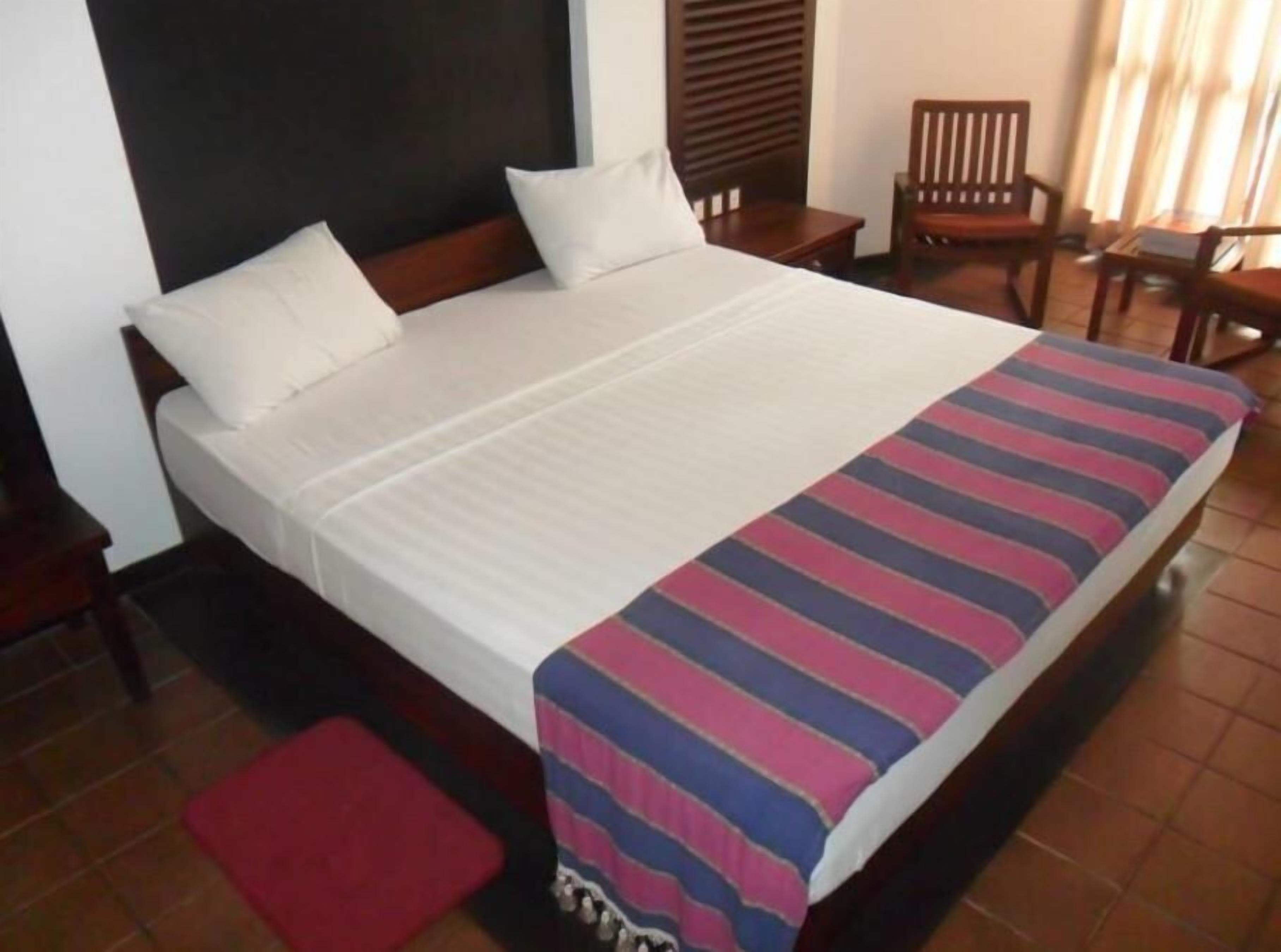 A hotel room with a large bed, wooden headboard, and a red bench.
