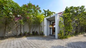 Ein gepflasterter Innenhof mit einem modernen Gebäudeeingang, umgeben von üppigem Grün und blühenden Pflanzen.