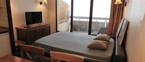 A hotel room with a bed, a desk, a television, and a balcony with a view.