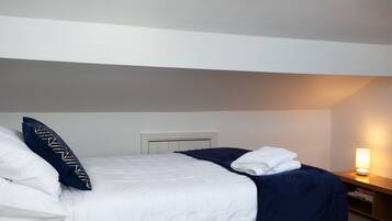 A hotel room with a bed, pillows, a bedside table with a lamp, and a wall-mounted heater.