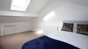 A bedroom with a sloped ceiling, a skylight, a bed with a white and dark blue duvet, and a radiator.