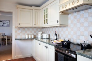 A kitchen with white cabinets, a granite countertop, a stove, and a dining area with a table and chairs. - Spacious 3 bedroom Cottage in Whalley (Whalley)