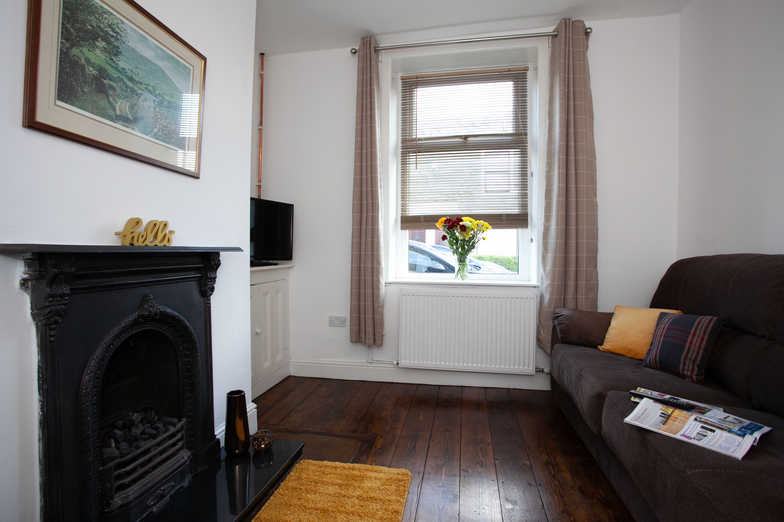A living room with a fireplace, a sofa, a television, and a window with curtains.