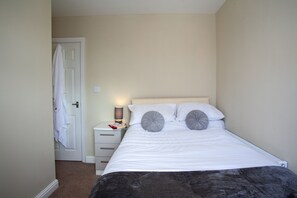 A bedroom with a bed, a nightstand, a lamp, and a door. - Spacious 3 bedroom Cottage in Whalley (Whalley)