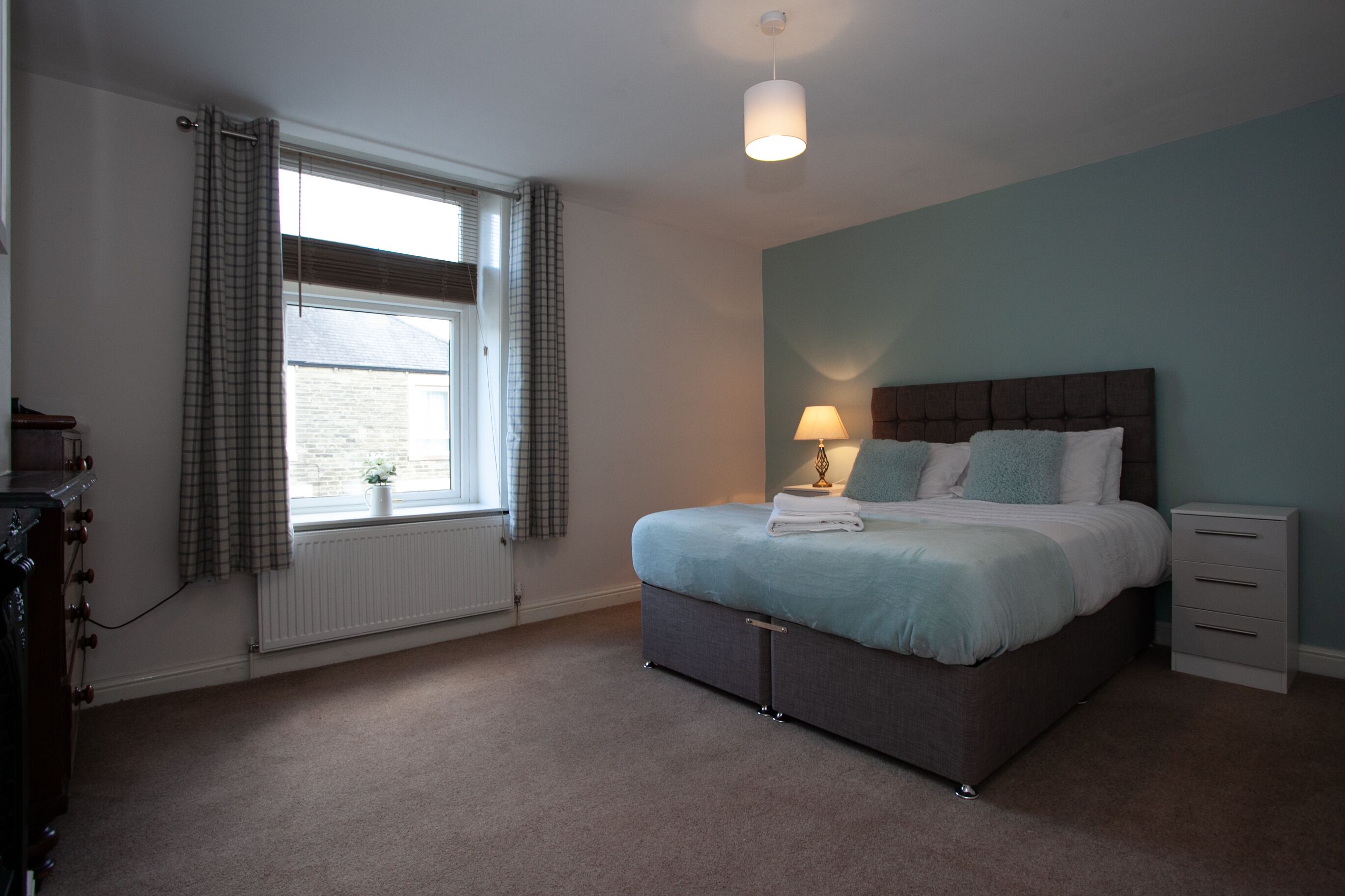 A bedroom with a bed, bedside table, lamp, and a window with curtains.