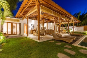 Relax in a serene outdoor space with lounge chairs and a hanging chair, surrounded by a lush lawn and a stone pathway leading to a pool.