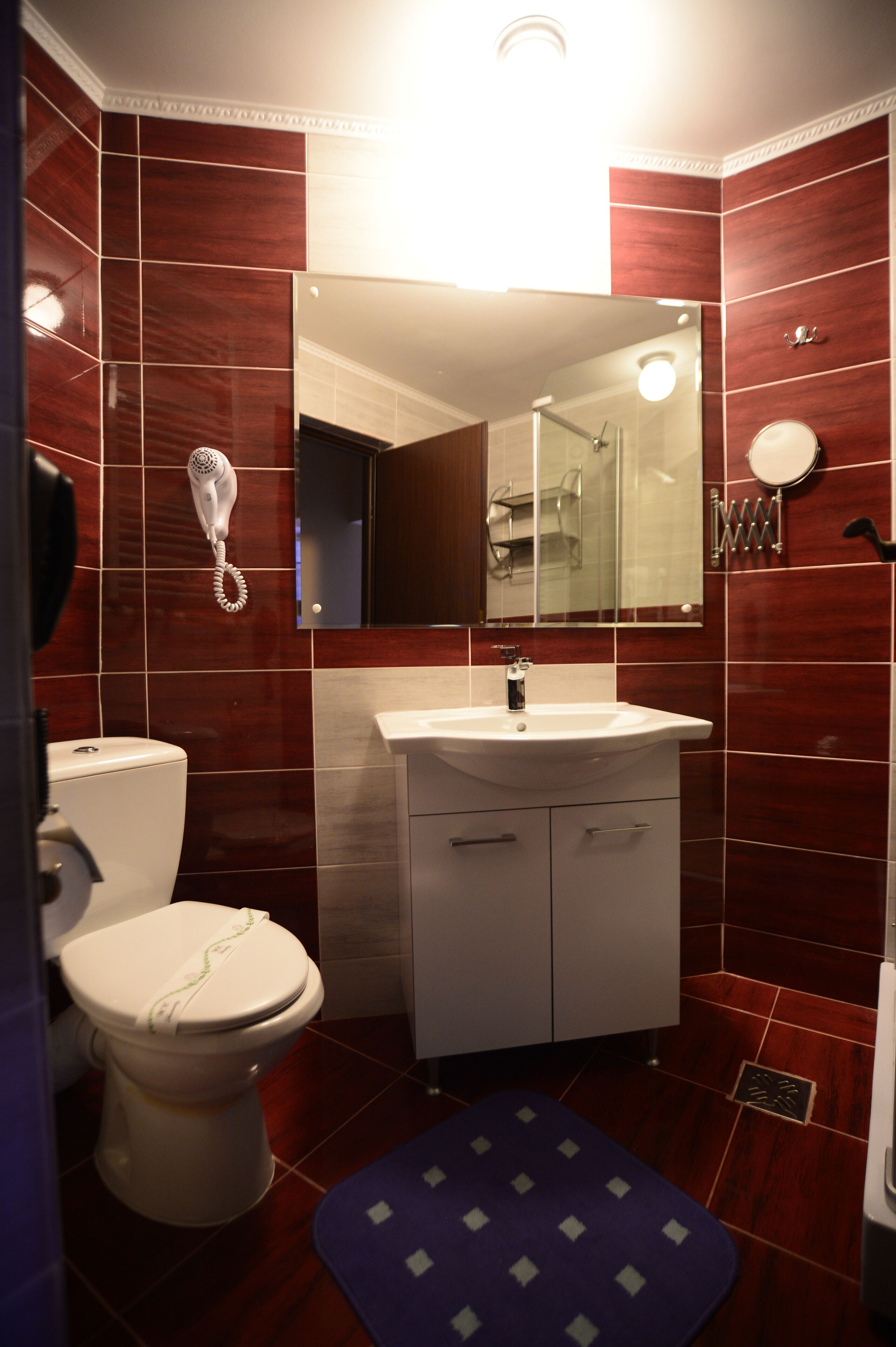 A bathroom with a toilet, sink, mirror, and a hairdryer on the wall.