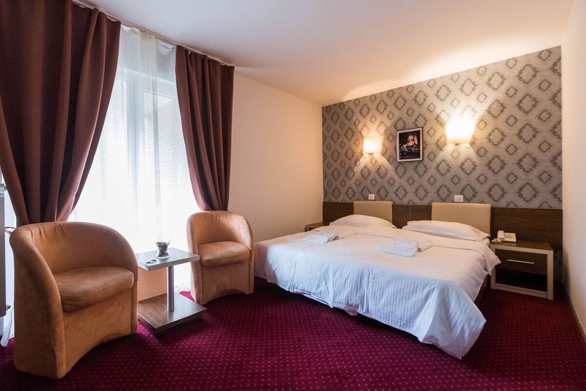 Habitación de hotel con una cama, dos sillas, una mesita y una mesita de noche.