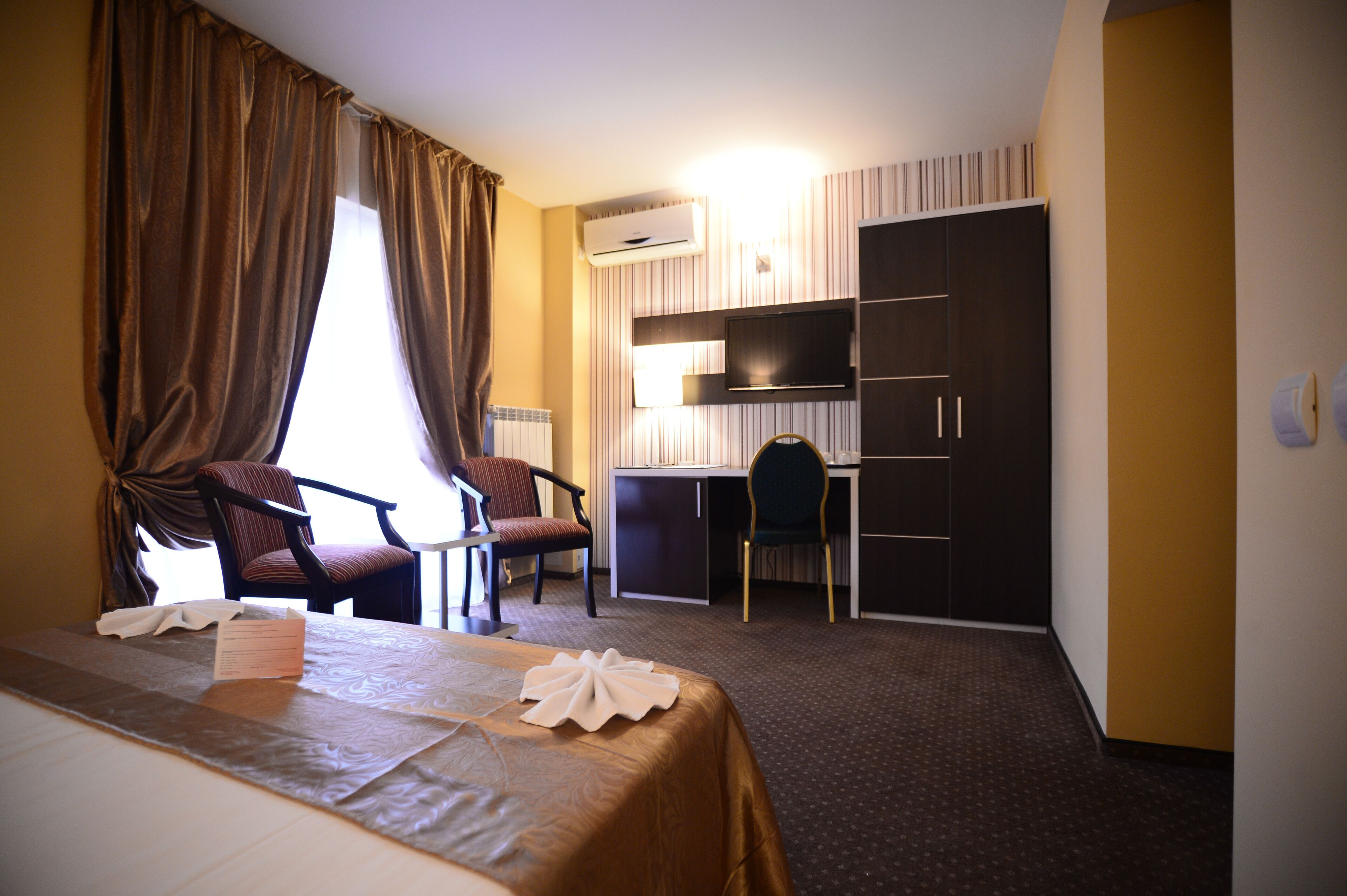A hotel room with a bed, two chairs, a desk, and a wardrobe.