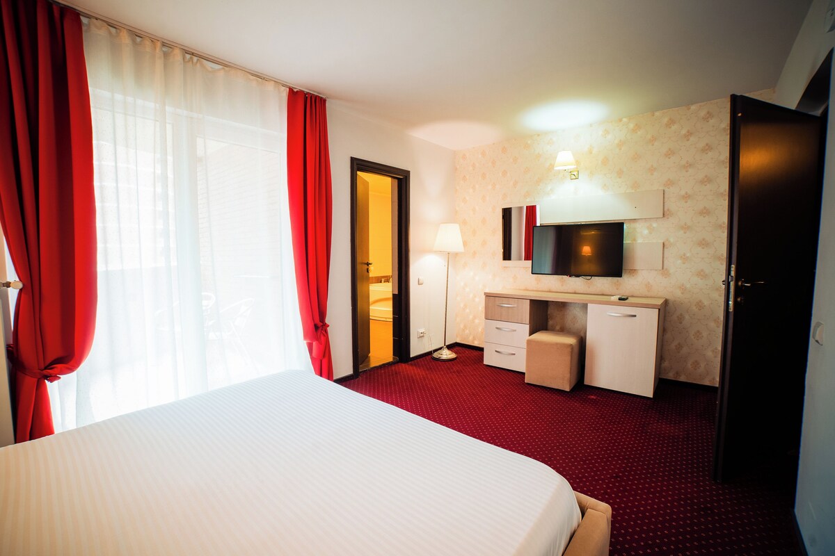 A hotel room with a bed, a desk, a mirror, a lamp, and a wardrobe.