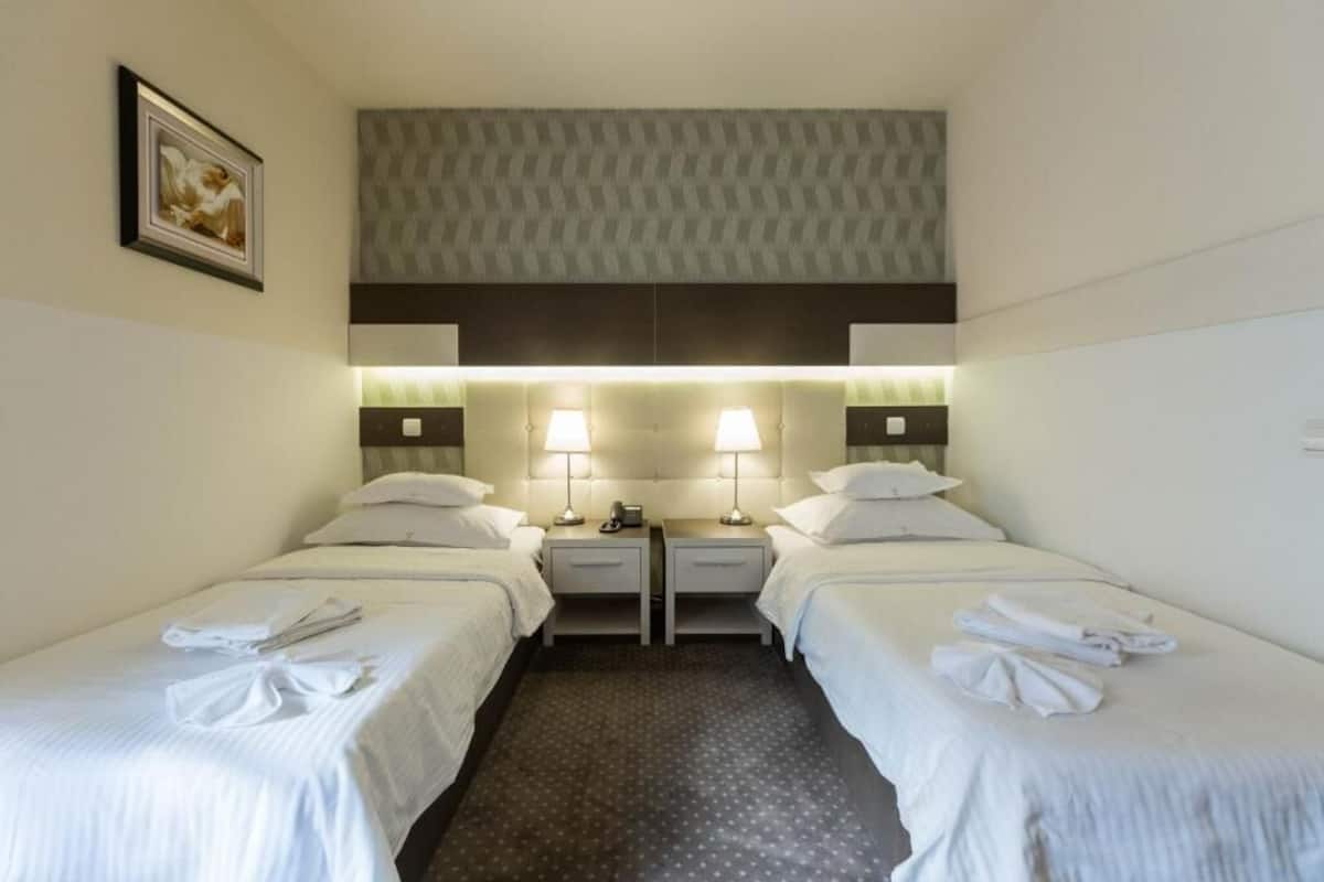 Una habitación de hotel con dos camas, cabeceras, lámparas de noche y un cuadro en la pared.