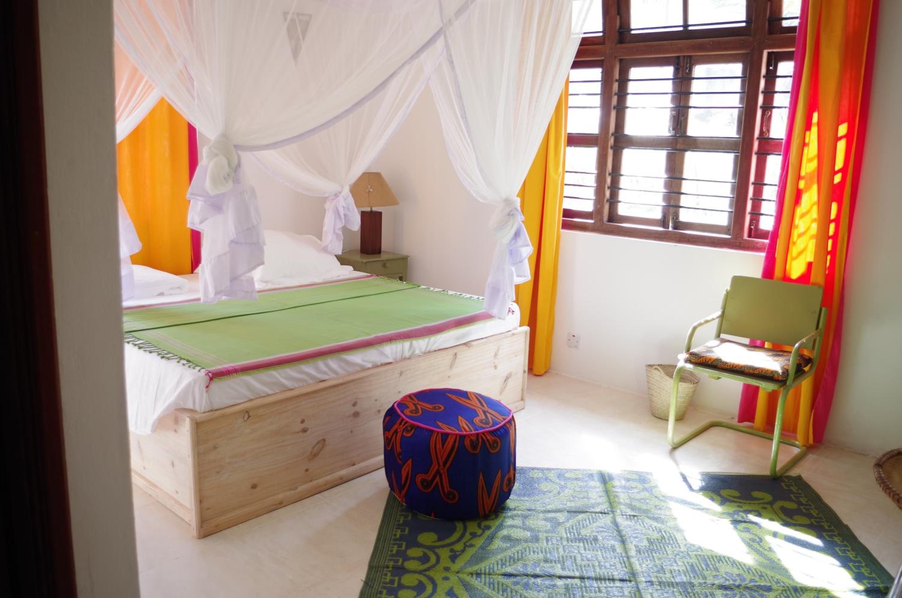 Una habitación con cama, una silla, un ventanal y una mesita de noche.