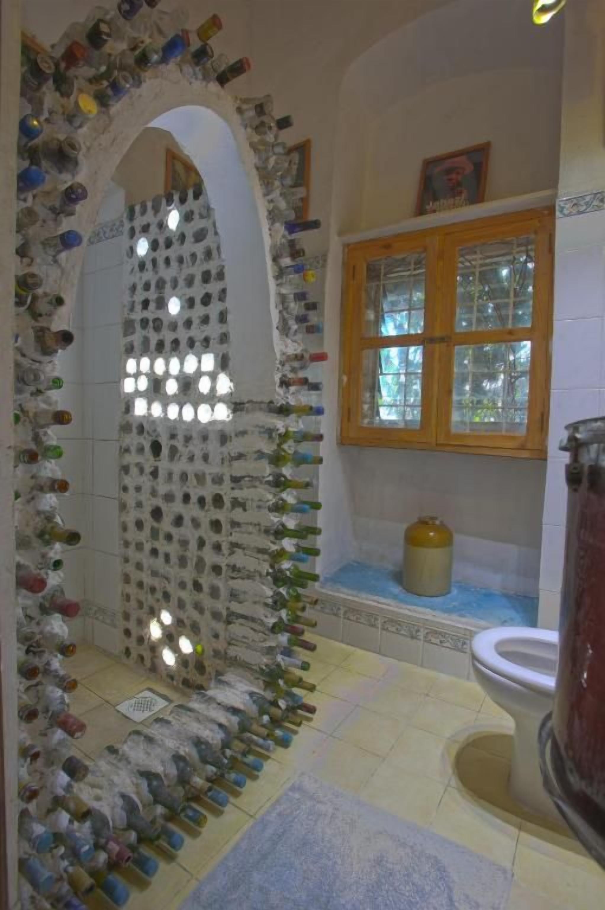 Ein Badezimmer mit einem einzigartigen Wanddesign aus Flaschen, einem Holzkabinent und einer Toilette.