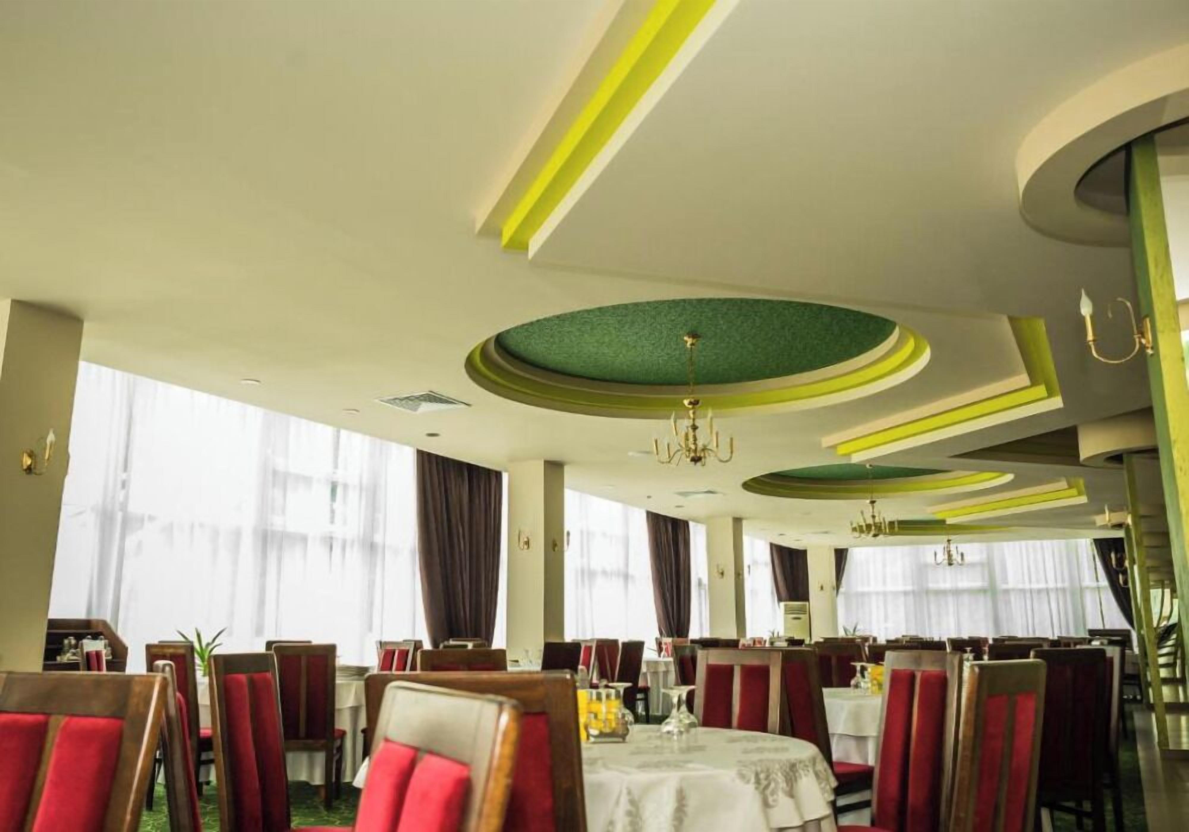 Un restaurante con mesas redondas, sillas tapizadas en rojo y un diseño de techo circular verde.